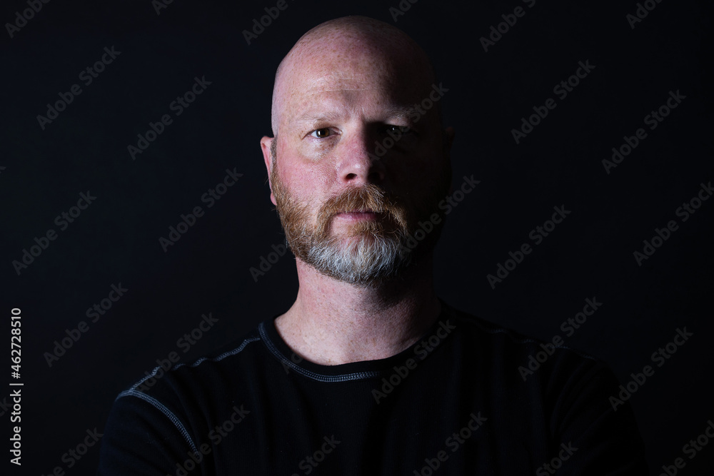 Dark portrait of a bald man with graying beard