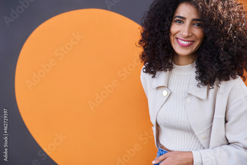 Smiling beautiful woman with curly hair standing against wall photo