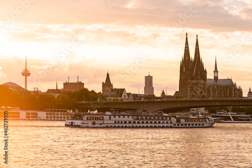 Germany, North Rhine-Westphalia, Cologne, Setting sun illuminating tourboat approaching Deutz Suspension Bridge photo