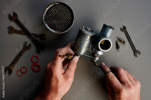 Top view of hand with vintage carburetor and tools in front of grey background photo