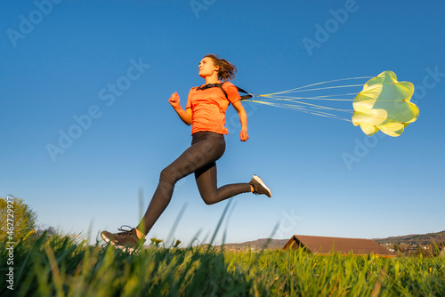 Low angle view of young woman sprinting with parachute against clear blue sky