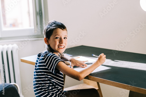 A middle school autism boy is doing his homework at home. The autism boy sits at the table and writes in a notebook at home. Aspeger syndrome and autism invisible diseases everyday life photo