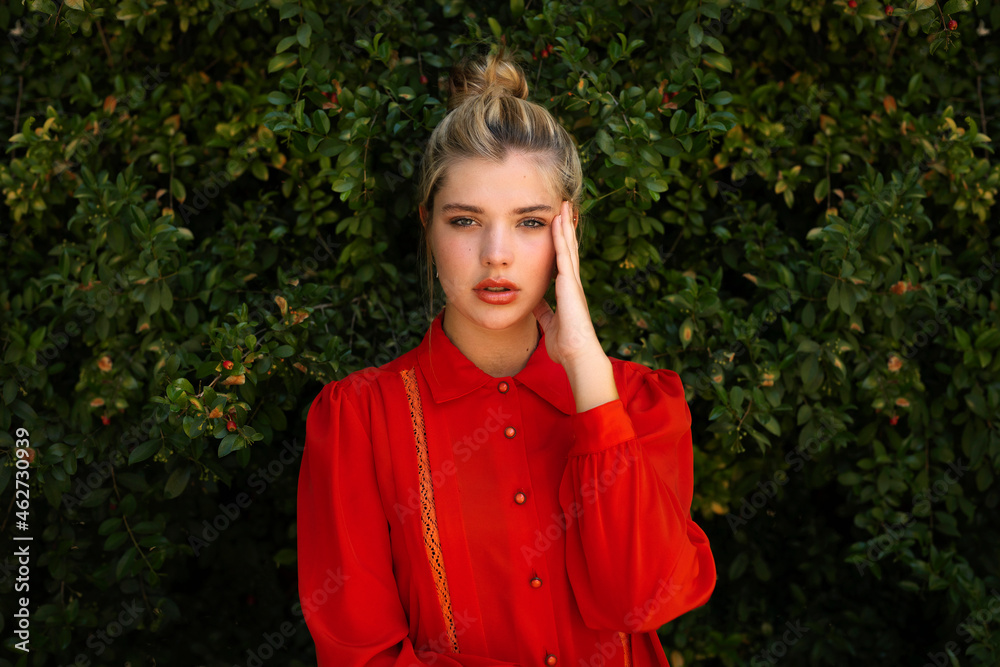 Beautiful woman in red shirt with head in hand standing against plants