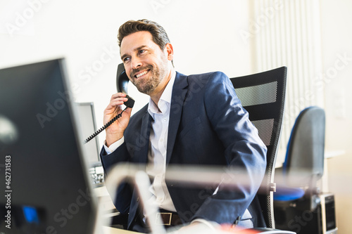 Smiling businessman talking on telephone while sitting on chair at office