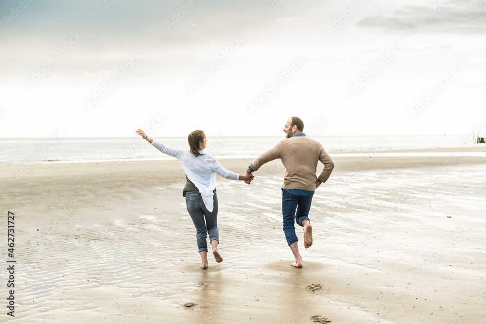 Cheerful couple holding hands while running at beach during sunset Cheerful couple holding hands while running at beach during sunset