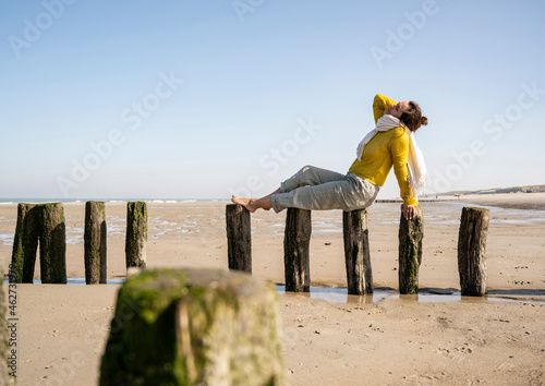 Woman sitting on wooden post at beach against clear sky photo