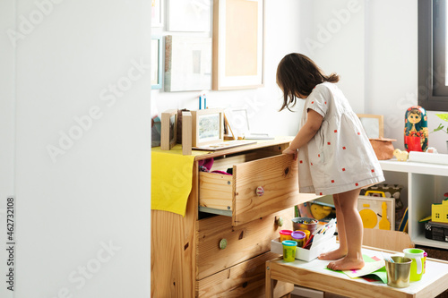 Cute girl searching in drawer while standing on table in playroom at home
