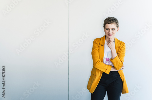Thoughtful female entrepreneur wearing yellow blazer standing against wall in office photo