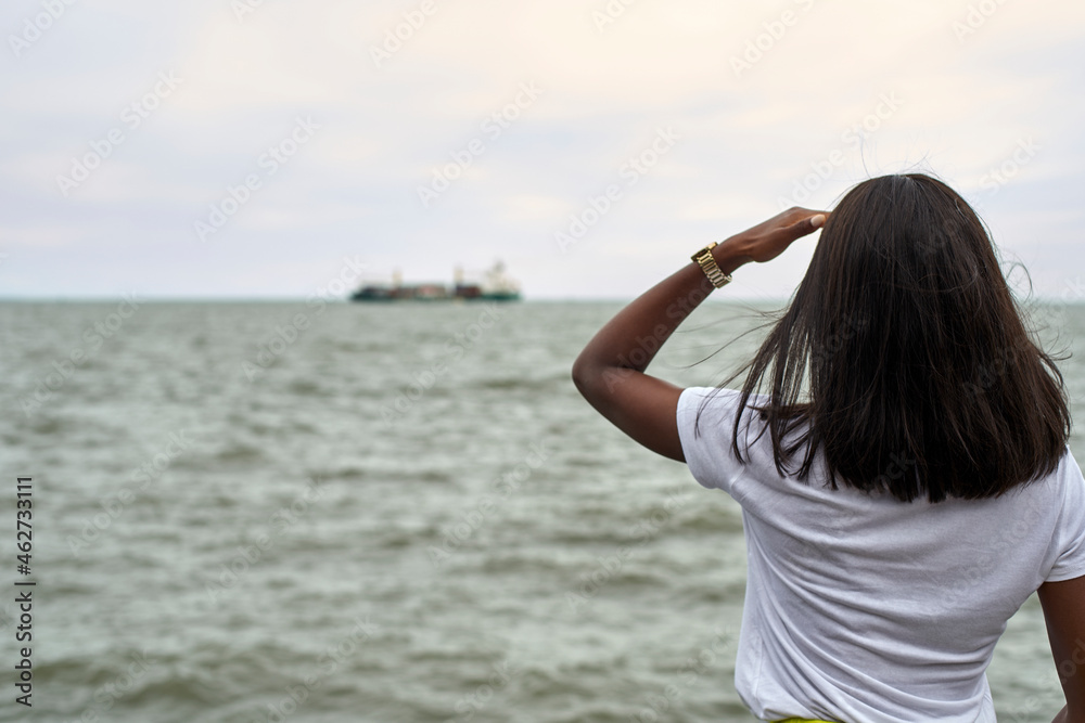 Back view of young woman in front of the sea looking to ship at horizon Back view of young woman in front of the sea looking to ship at horizon