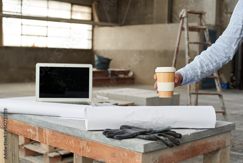 Hand of male architect placing coffee cup on table in building