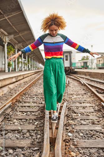 Full length of young woman with afro hairstyle walking on tracks at station against sky photo