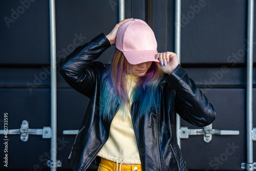 Portrait of young woman with dyed hair and baseball cap in front of black container photo