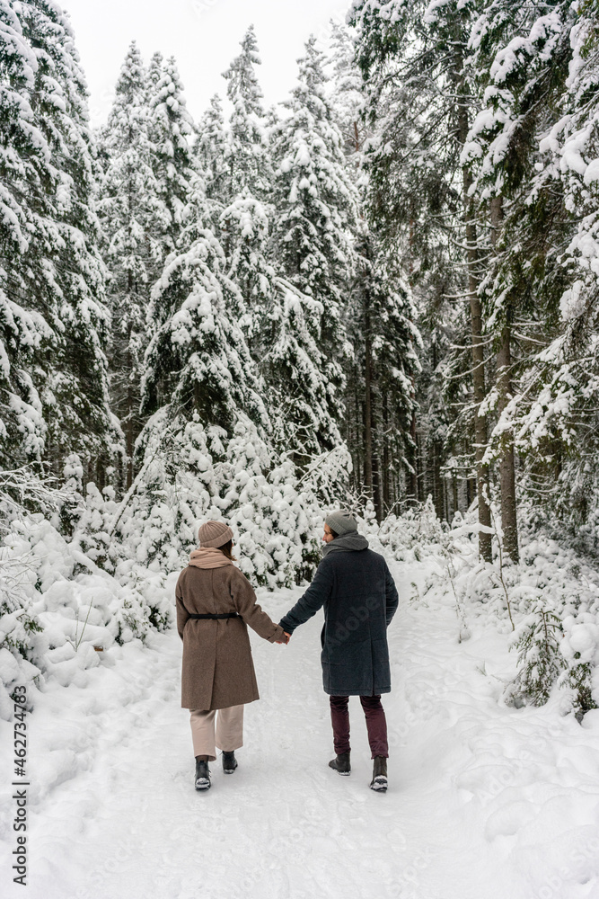 Couple holding hands while walking on snowy forest path Couple holding hands while walking on snowy forest path