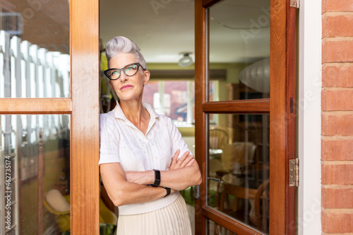 Contemplating senior woman with arms crossed standing on doorway at home photo