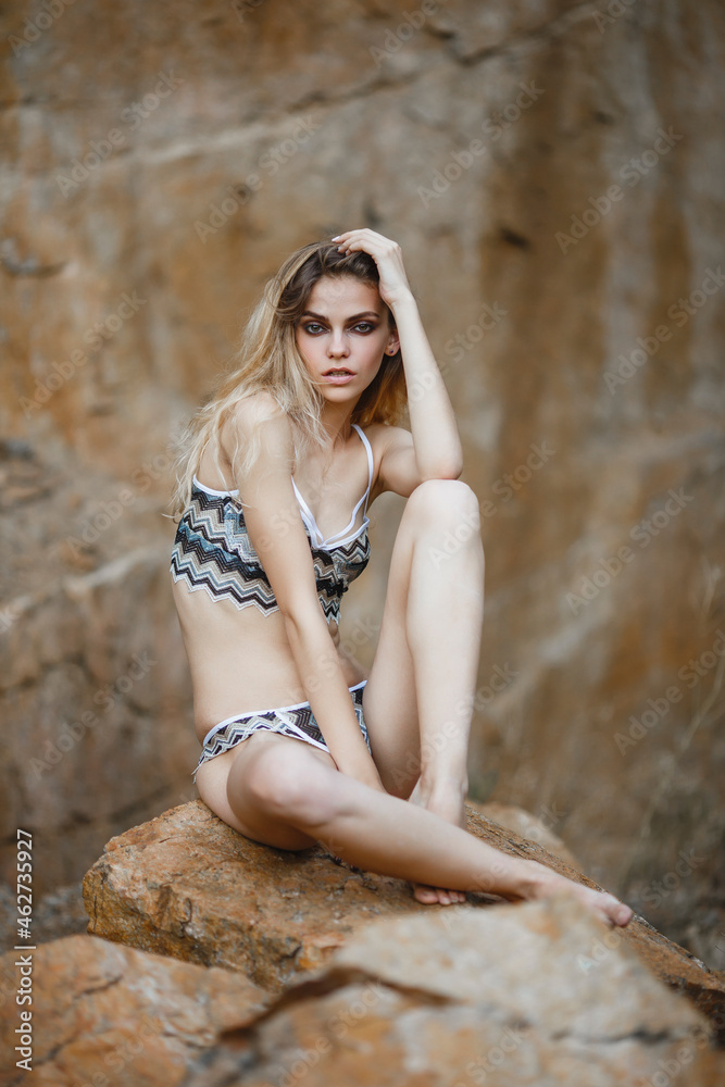 Obraz premium Young girl in bikini on the ocean shore. Stone background. Portrait of a Caucasian girl with European facial features.
