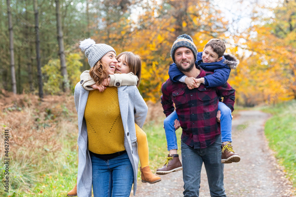 Parents piggybacking children while walking in forest during autumn Parents piggybacking children while walking in forest during autumn