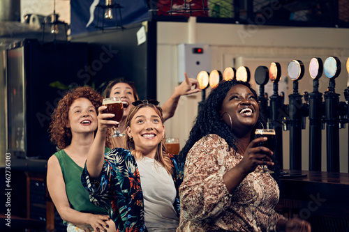 Excited female friends sitting at the counter in a pub watching Tv photo