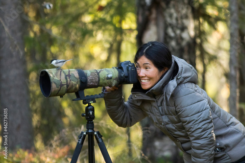Finland, Kuhmo, North Karelia, Kainuu, Smiling woman with willow tit (Poecile montanus) perching in camera lens in forest photo