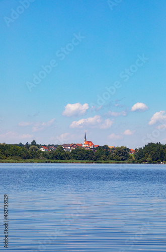 Germany, Bavaria, Leobendorf, Sky over blue water of Abtsdorfer See in summer with village in background photo
