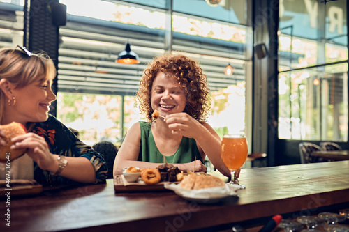 Two happy female friends having a snack at the counter in a pub
