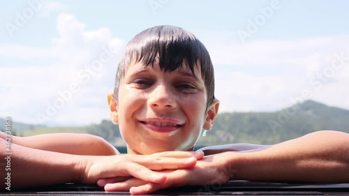 Portrait of boy smiling while leaning at edge of swimming pool against sky