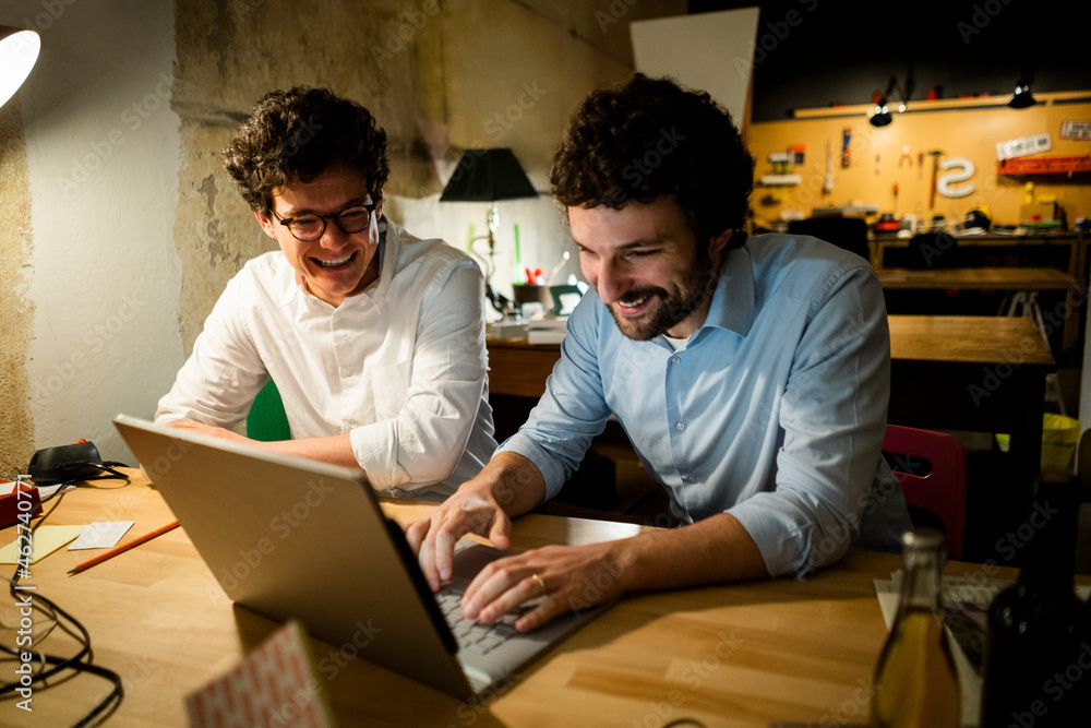 Two happy colleagues using laptop in the dark together