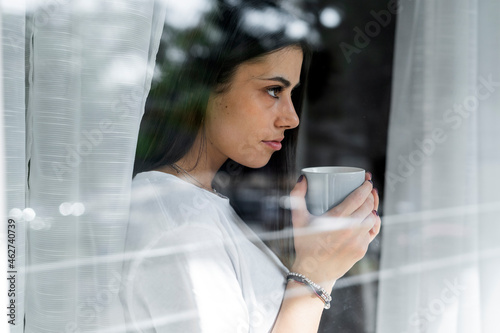 Young woman with cup of coffee behind windowpane photo