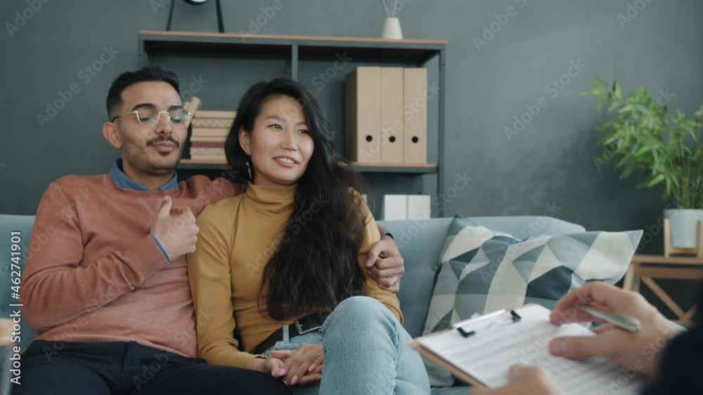 Joyful young husband and wife are talking during counseling session with professional therapist in modern office. People and therapy concept. Joyful young husband and wife are talking during counseling session with professional therapist in modern office. People and therapy concept.