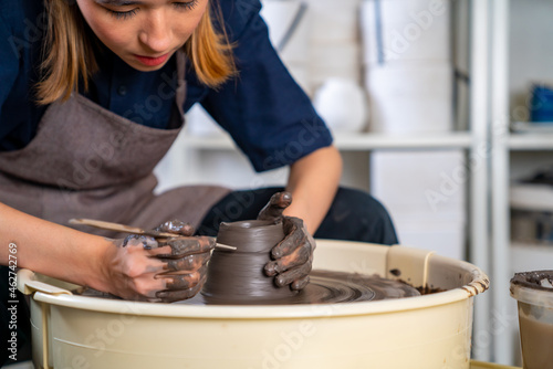  Asian woman sculptor artist hands sculpture clay on pottery wheel at ceramic studio. Female craftsman molding raw clay create pottery shapes at workshop. Small business handicraft product concept.