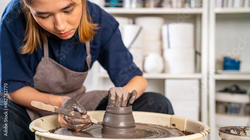  Asian woman sculptor artist hands sculpture clay on pottery wheel at ceramic studio. Female craftsman molding raw clay create pottery shapes at workshop. Small business handicraft product concept.