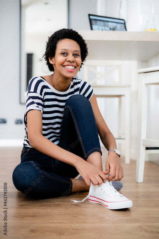 Portrait of happy young woman sitting on the floor at home lacing her sneakers Portrait of happy young woman sitting on the floor at home lacing her sneakers