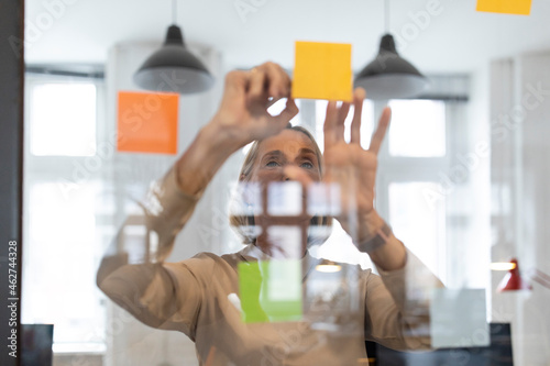 Mature businesswoman with adhesive notes on glass pane in office