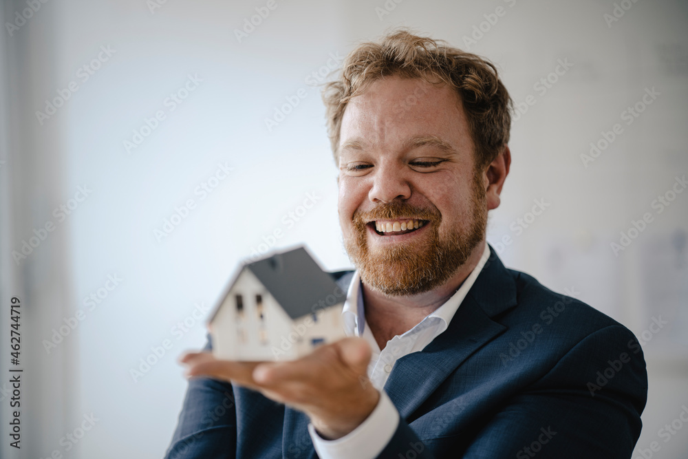 Happy businessman holding model house in office Happy businessman holding model house in office