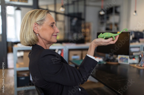 Mature businesswoman holding chameleon figurine in office