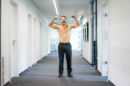 Screaming barechested businessman flexing muscles in office