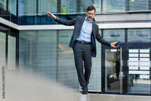 Mature businessman balancing on a wall outside office building photo