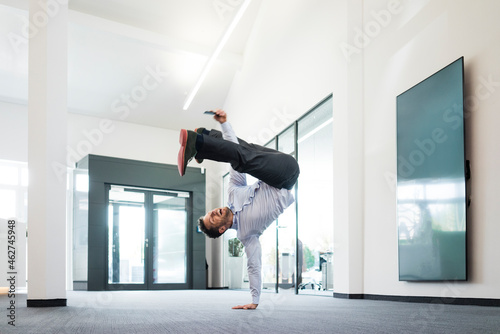 Businessman with cell phone doing a one-handed handstand on office floor photo