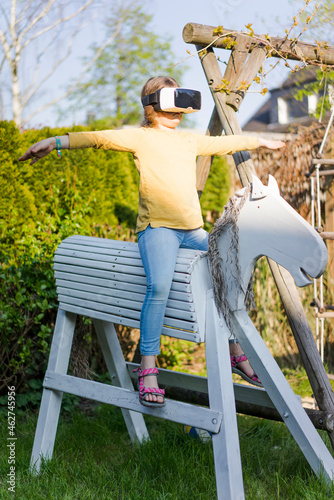 Girl practicing on wooden horse in garden wearing VR glasses