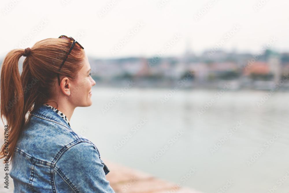Young redhead woman looking into distance at riverside