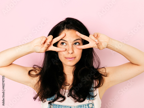 Portrait of young smiling woman with black hair and hands on face, in front of pink background photo