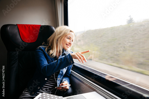 Smiling blond woman travelling by train looking out of window photo