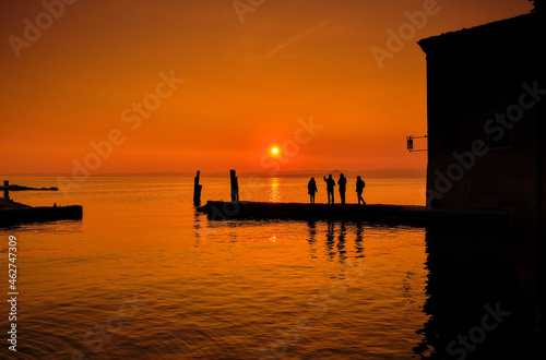 Italy, Punta san Vigilio, silhouettes of four people on jetty watching sunset over Lake Garda in winter photo