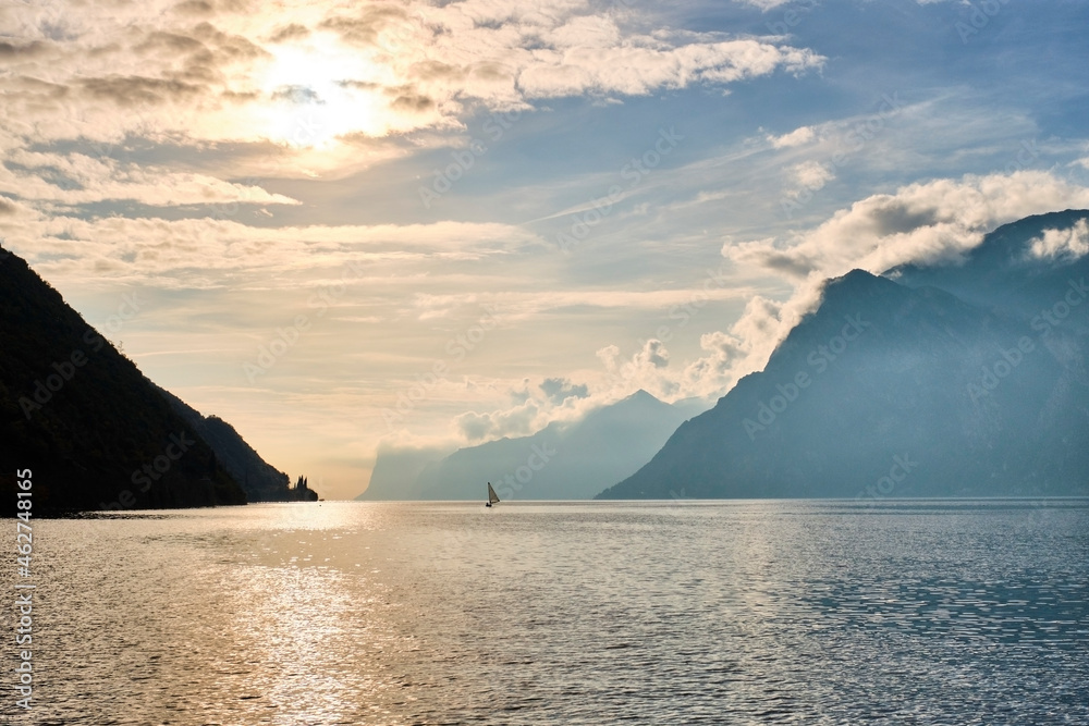 Italy, Trentino, Nago-Torbole, Silhouette of sailboat sailing near coastal cliffs of Lake Garda at moody sunrise Italy, Trentino, Nago-Torbole, Silhouette of sailboat sailing near coastal cliffs of Lake Garda at moody sunrise
