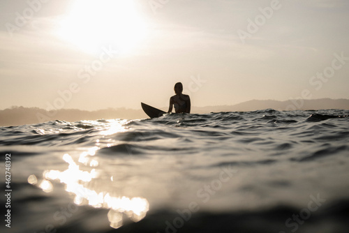 Female surfer sitting on surfboard in the evening, Costa Rica