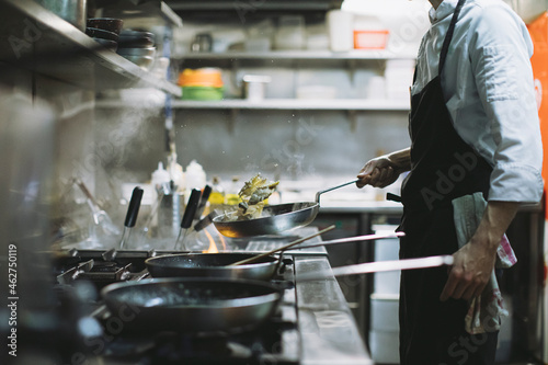Chef preparing a dish at gas stove in restaurant kitchen photo