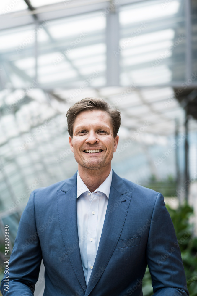 Smiling businessman standing i n green atrium, portrait Smiling businessman standing i n green atrium, portrait