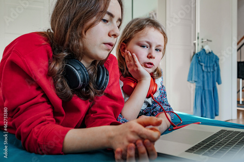 Portrait of two sisters with headphones and laptop on bed photo