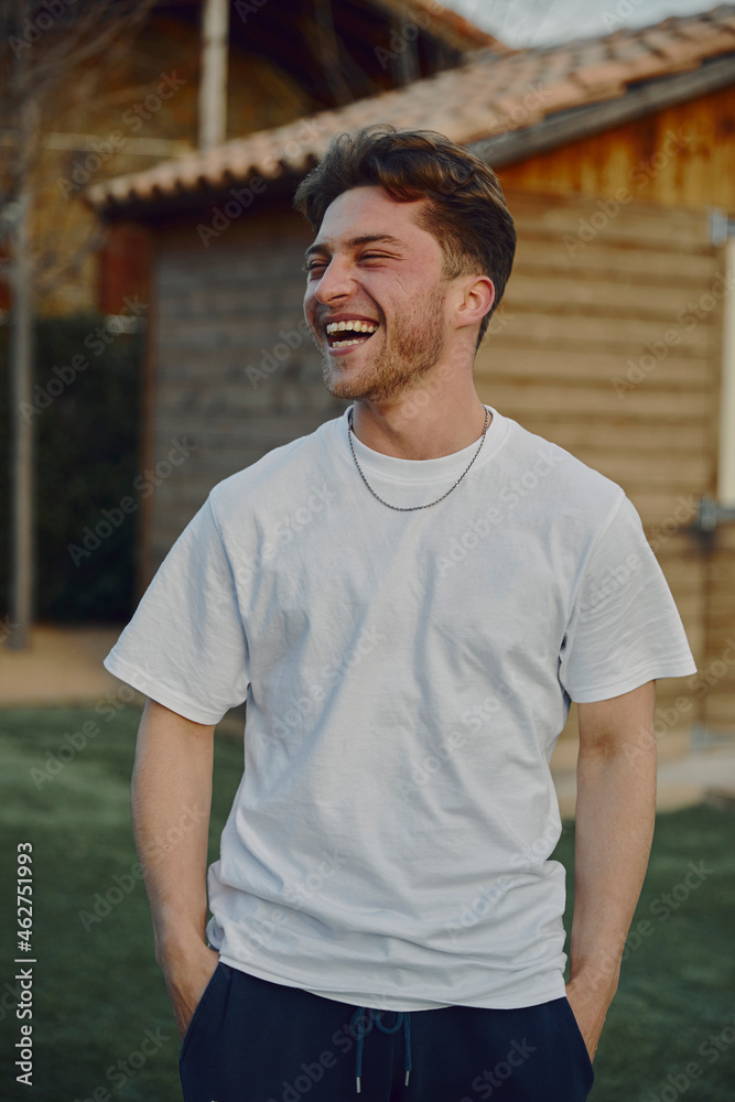 Laughing handsome man with hands in pockets standing by house Laughing handsome man with hands in pockets standing by house