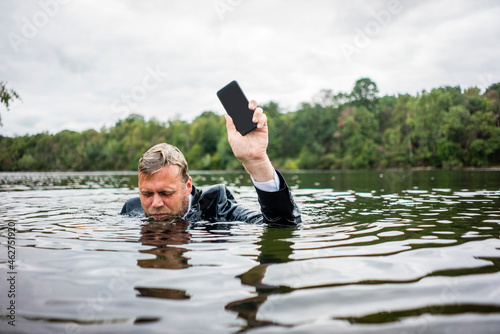 Businessman holding cell phone inside a lake photo
