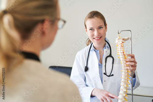 Female doctor explaining spine model to patient in medical practice photo